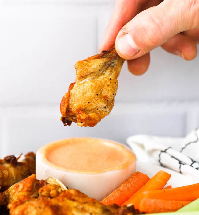 Small chicken drumstick held in a hand over dipping sauce