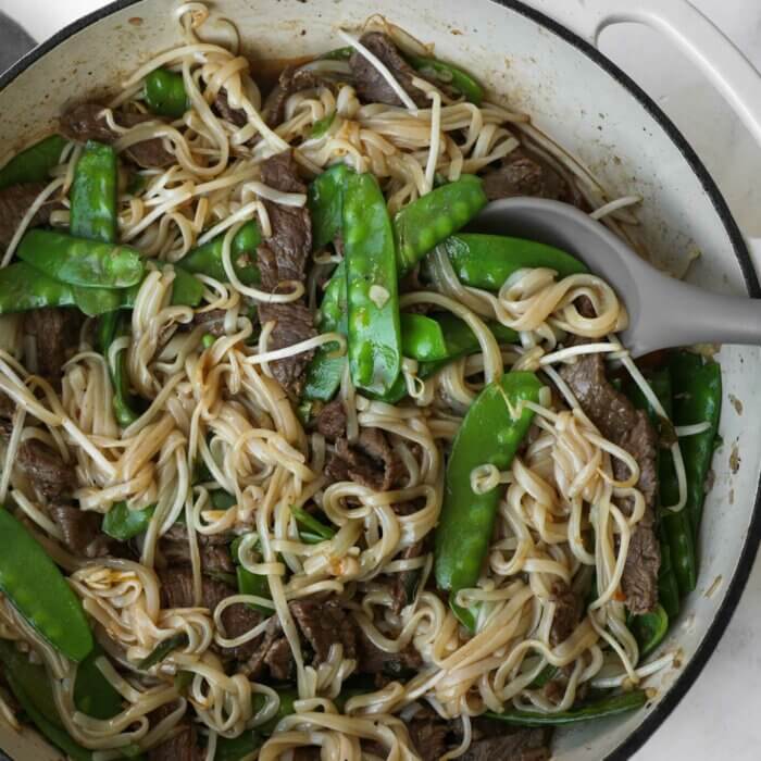 Close up overhead shot of beef pad thai with snow peas and a spoon sticking out.