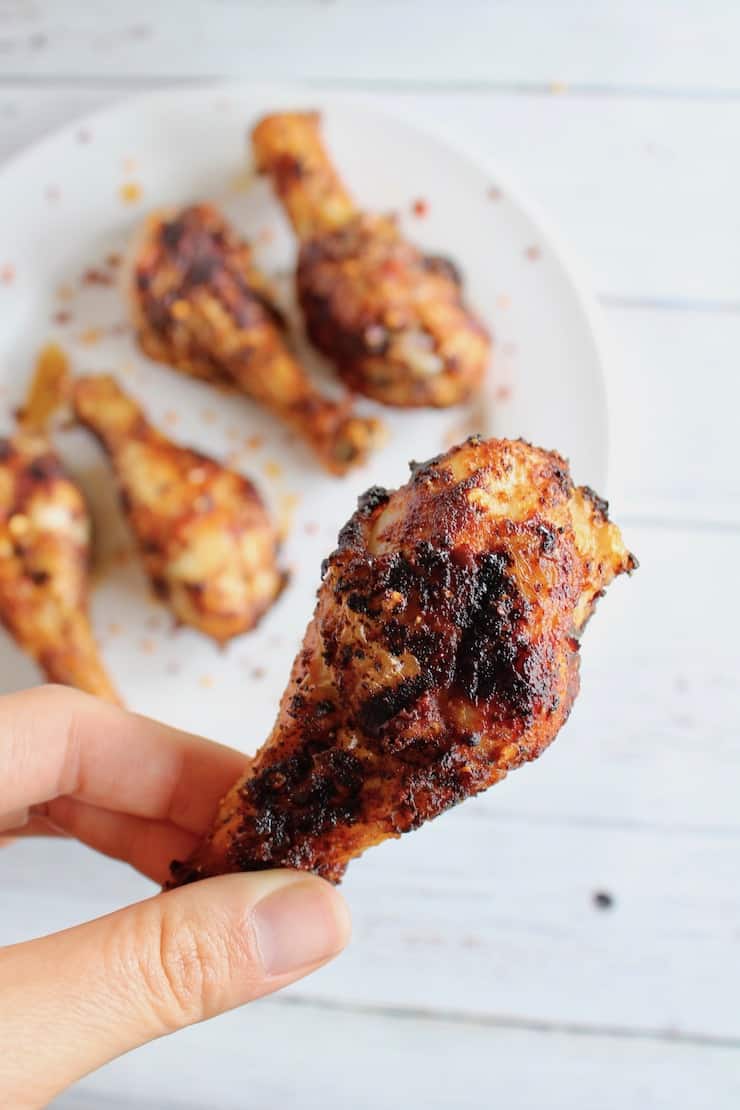 Hand holding cooked air fryer chicken leg with legs on plate in the background