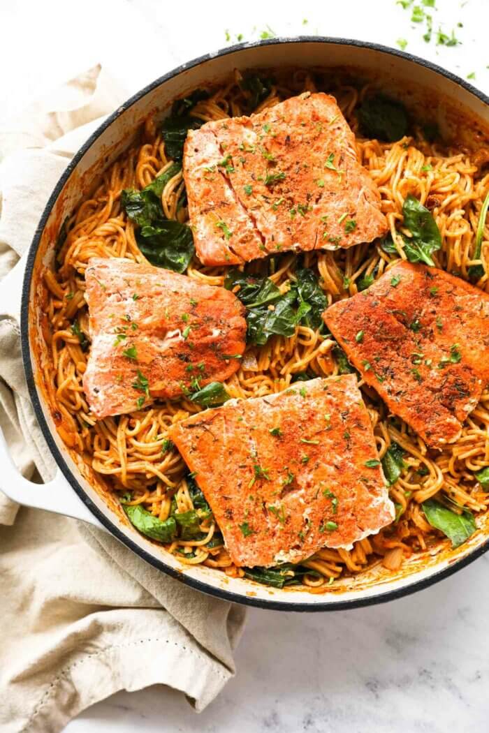 Close up overhead image of a skillet filled with pasta and four cajun salmon filets.