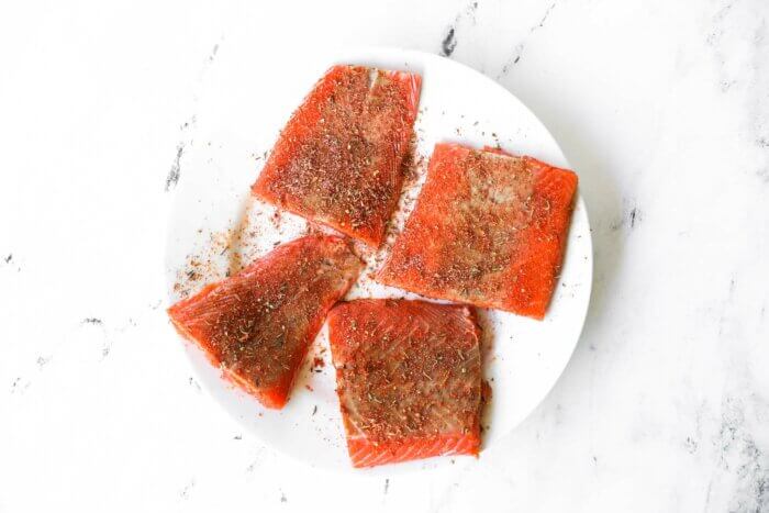 Four raw salmon filets on a plate covered in homemade cajun seasoning mix.