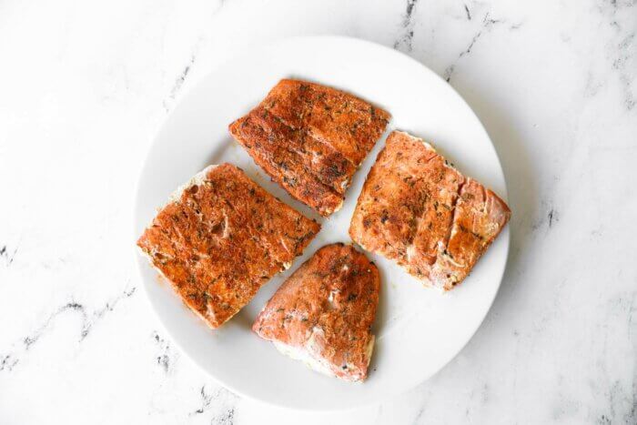 Four cooked salmon filets on a plate.