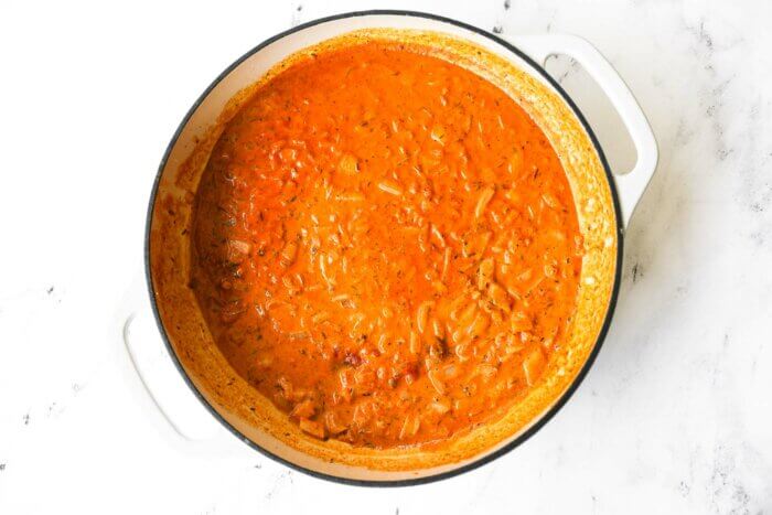 Orange/red creamy cajun salmon pasta sauce simmering in a skillet.