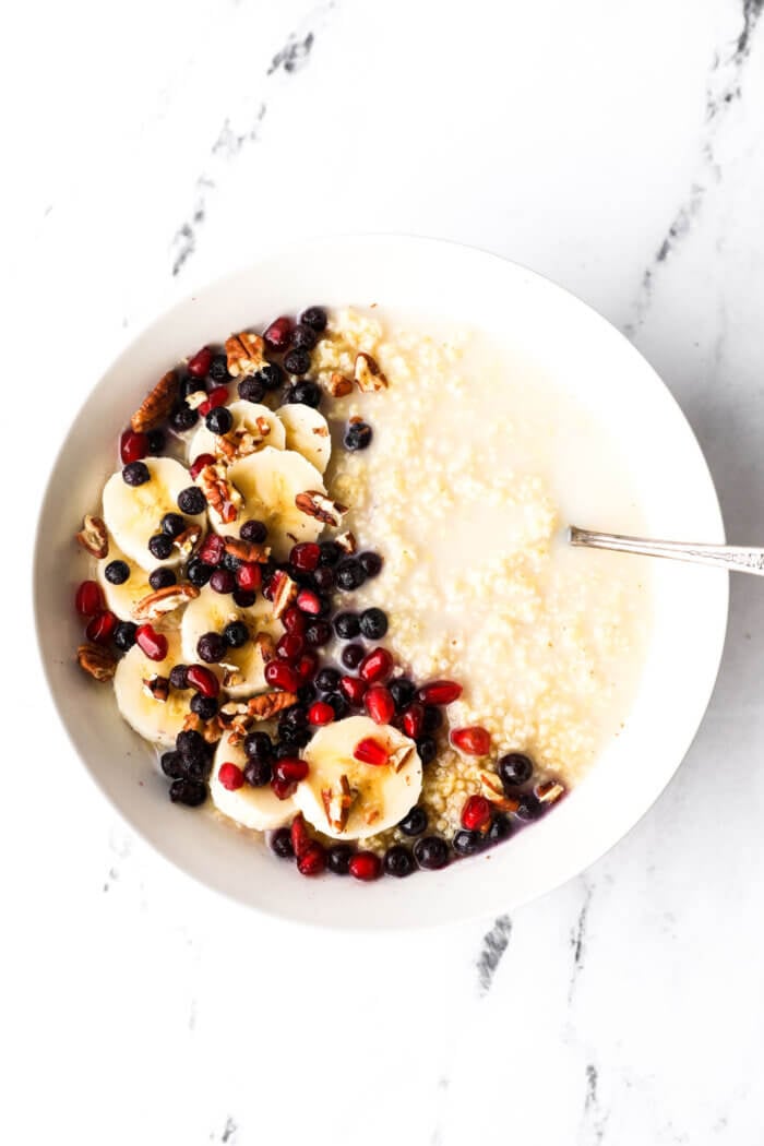 Bowl of creamy millet porridge with coconut milk, bananas, berries, pomegranate seeds and chopped pecans.