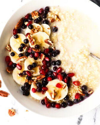 Close up image of a bowl of creamy millet porridge with coconut milk, bananas, berries, pomegranate seeds and chopped pecans.