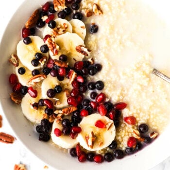 Close up image of a bowl of creamy millet porridge with coconut milk, bananas, berries, pomegranate seeds and chopped pecans.