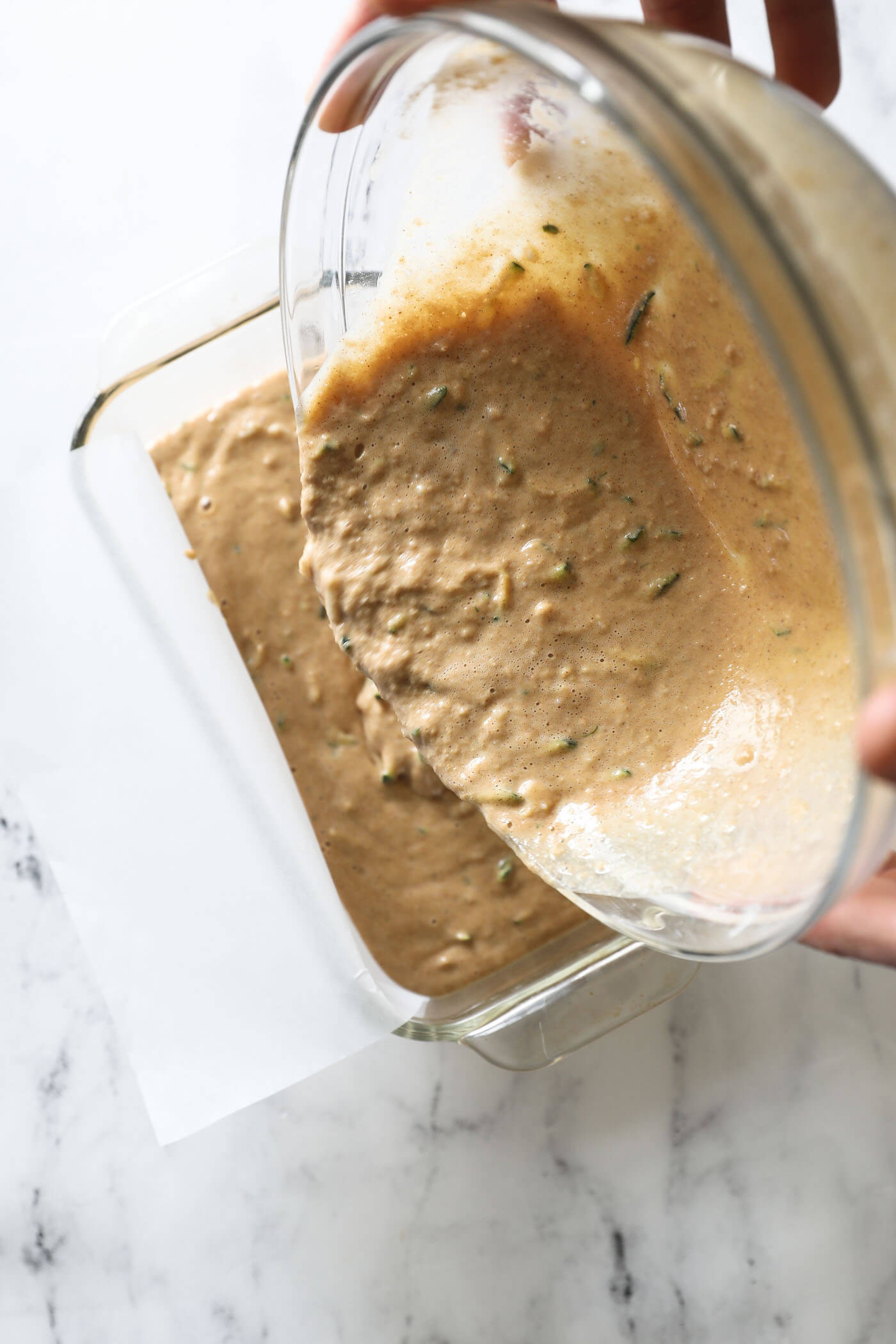 Pouring the batter into a parchment lined glass loaf pan.