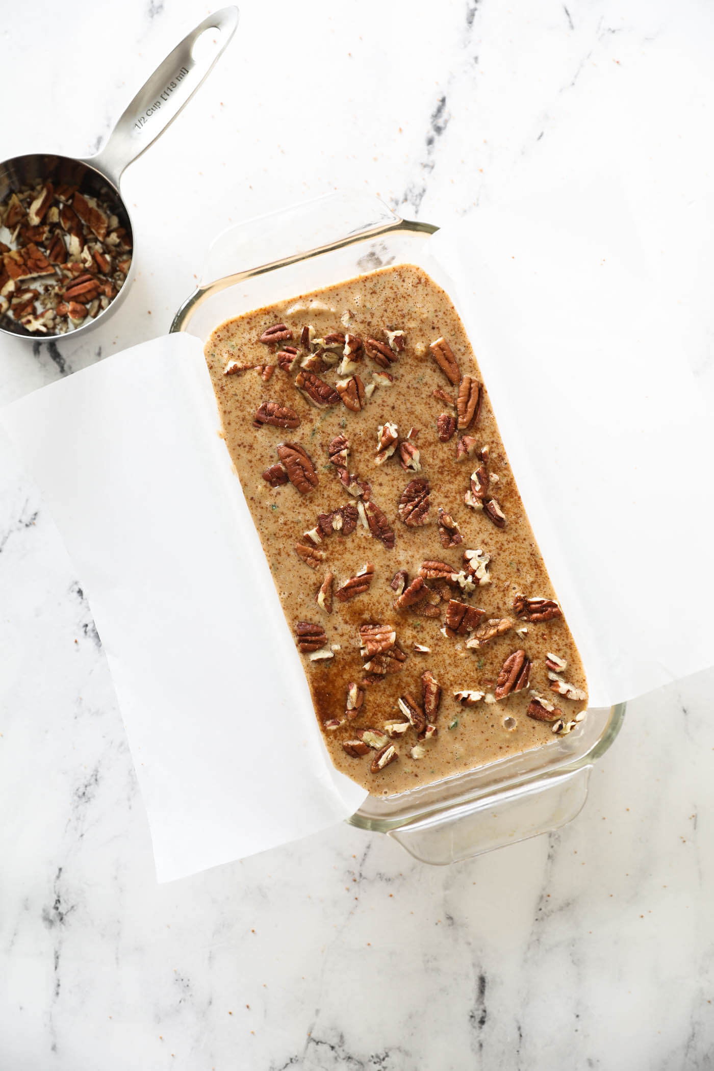 The uncooked batter in a loaf pan with chopped pecans and coconut sugar sprinkled on top.