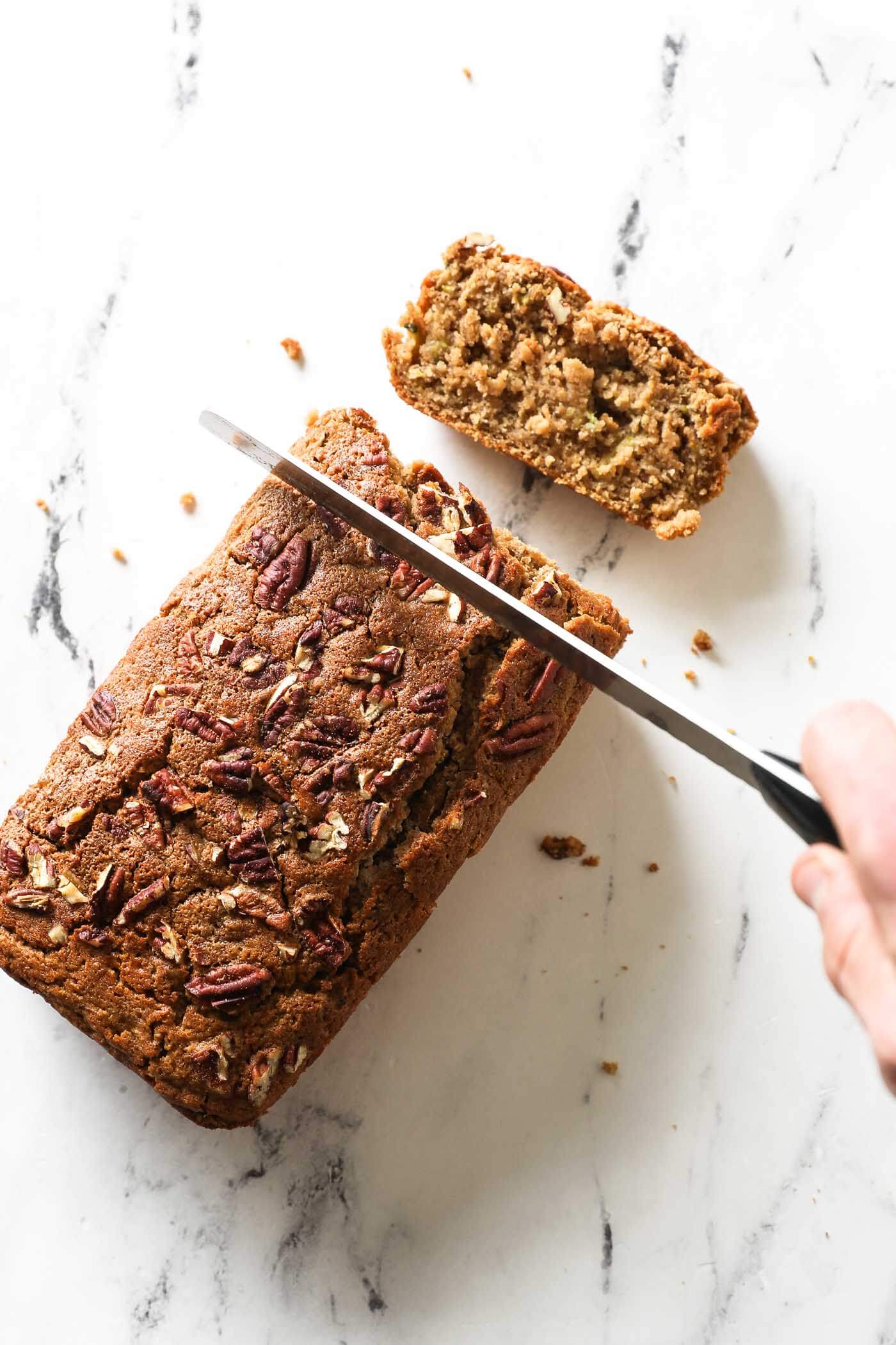 Overhead image of slicing a loaf of zucchini bread. One piece already sliced and to the side.