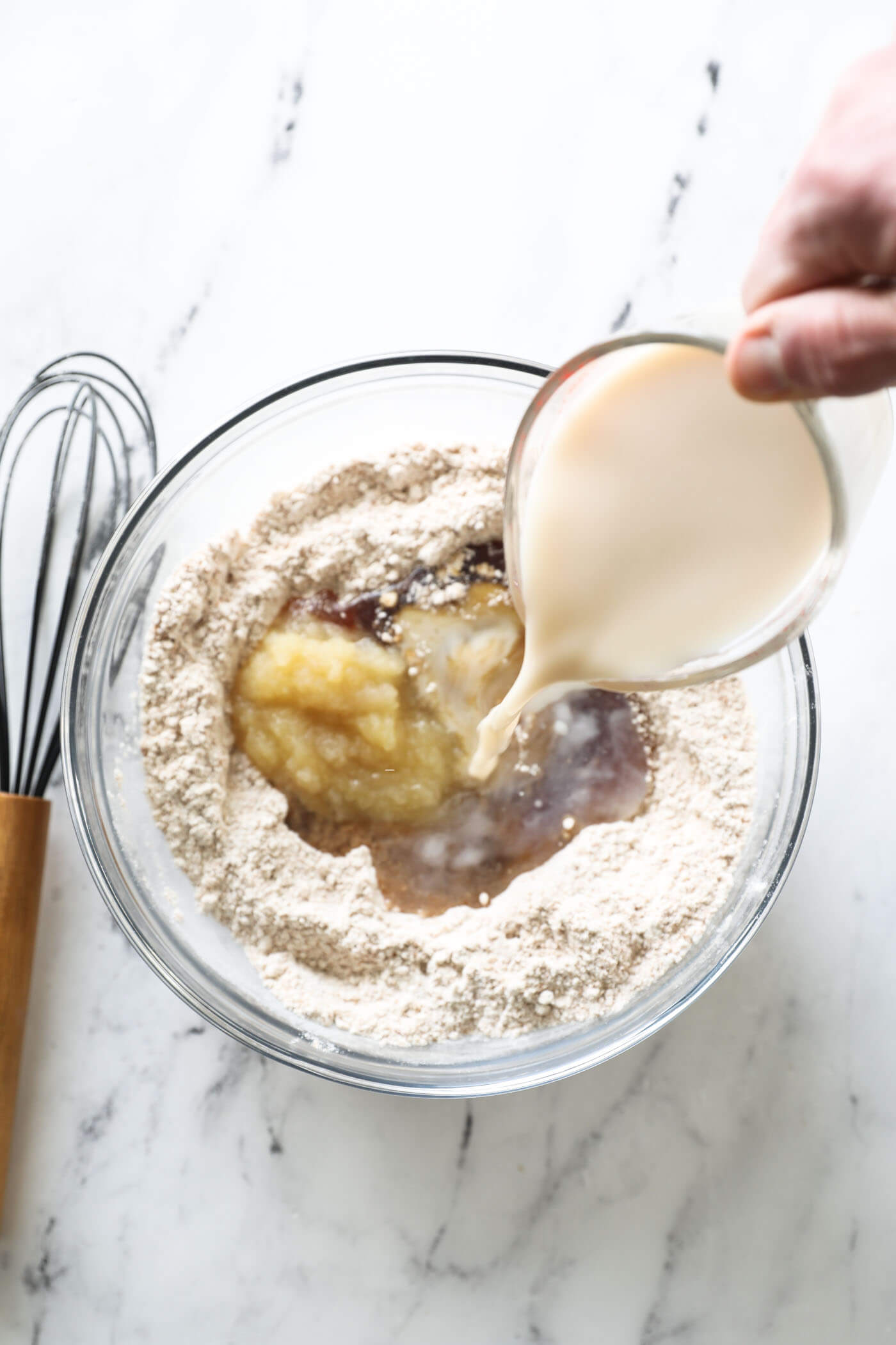 Pouring in almond milk to a mixing bowl with the ingredients to make zucchini bread.