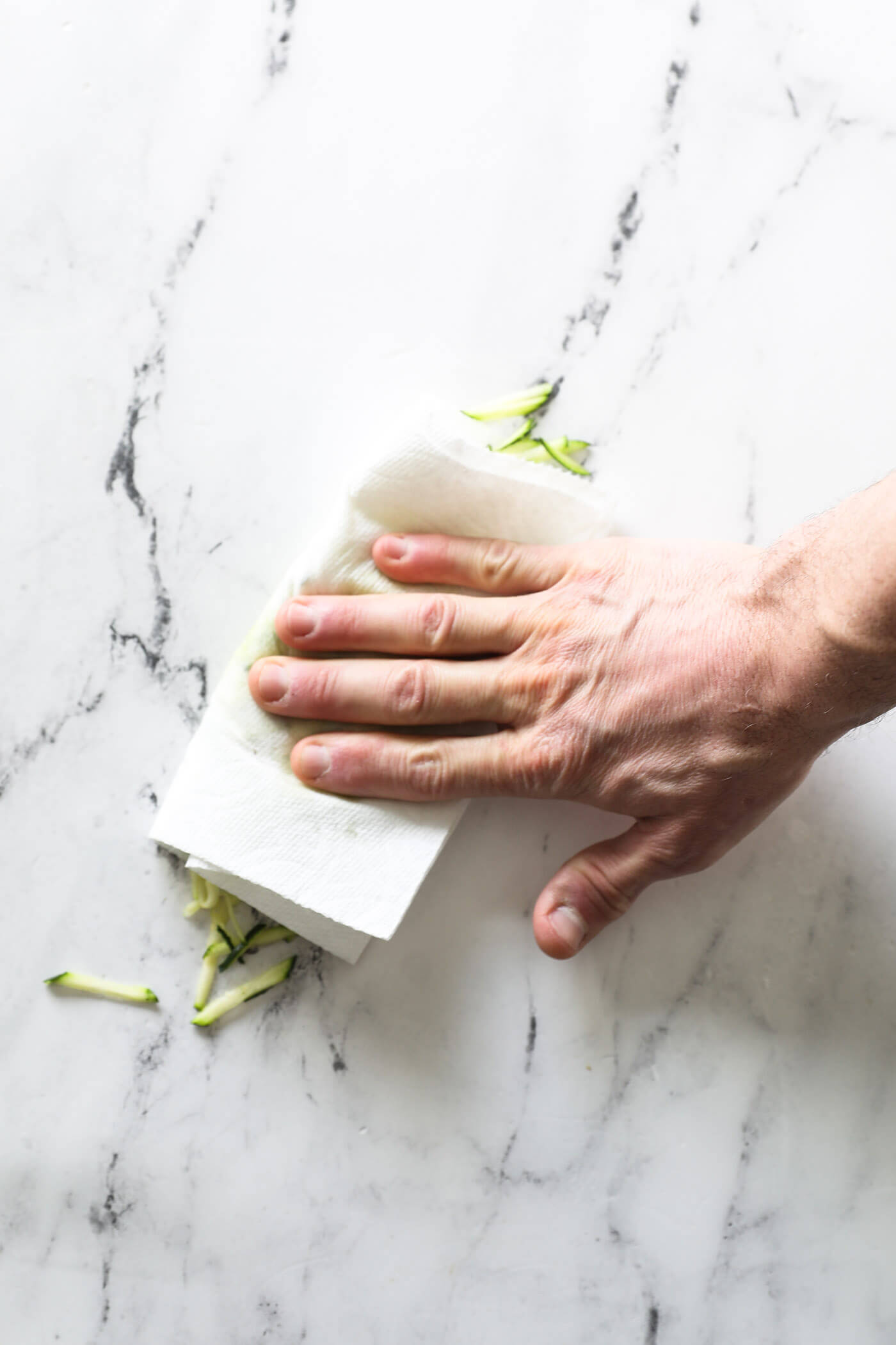 A hand patting shredded zucchini to get the excess liquid out.