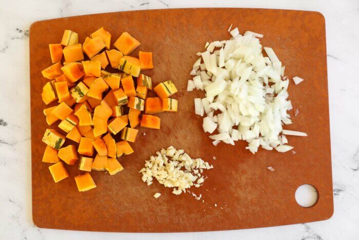Cubed delicata squash, minced garlic and chopped onion on a cutting board.