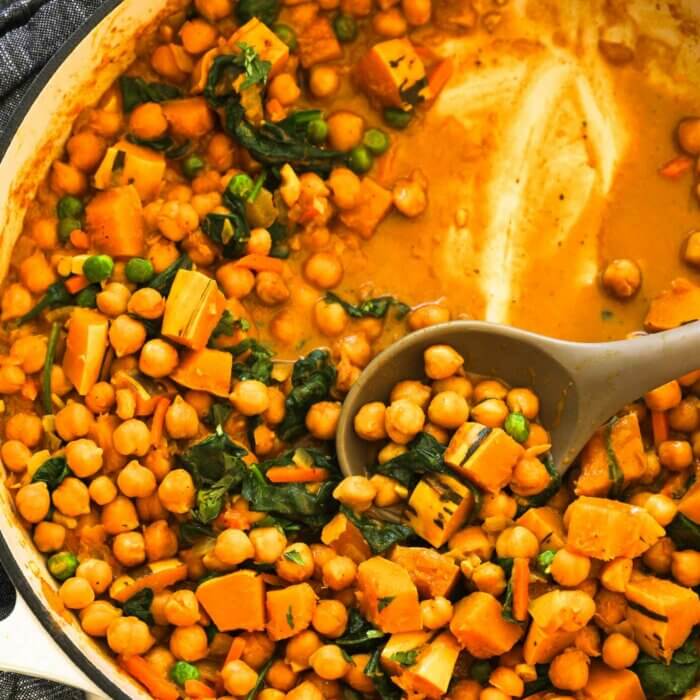 Creamy, chickpea and spinach curry in a skillet with a serving spoon dug in.