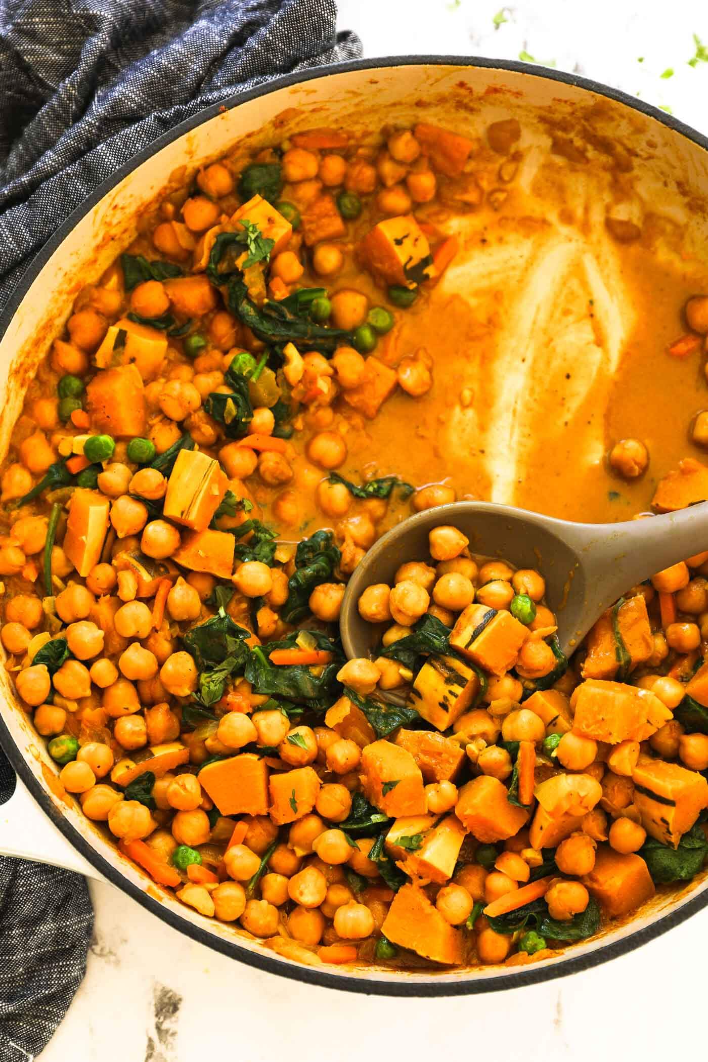 Creamy, chickpea and spinach curry in a skillet with a serving spoon dug in. 