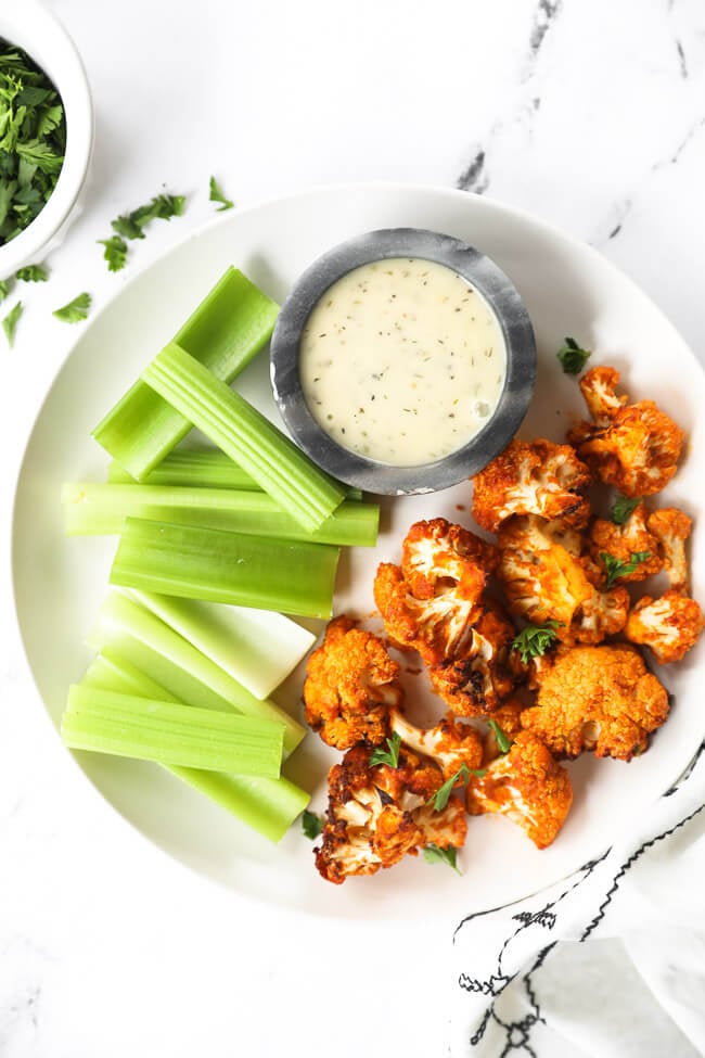 buffalo cauliflower bites on a white plate with celery sticks and ranch dressing on the side