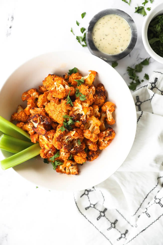 buffalo cauliflower bites in a bowl with celery sticks and ranch dressing on the side
