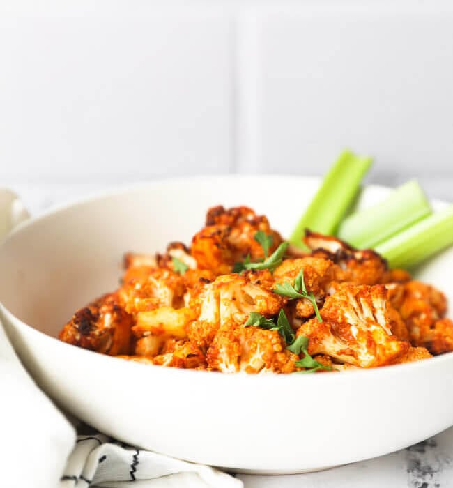 Air fryer buffalo cauliflower bites in a white bowl with celery sticks straight on image