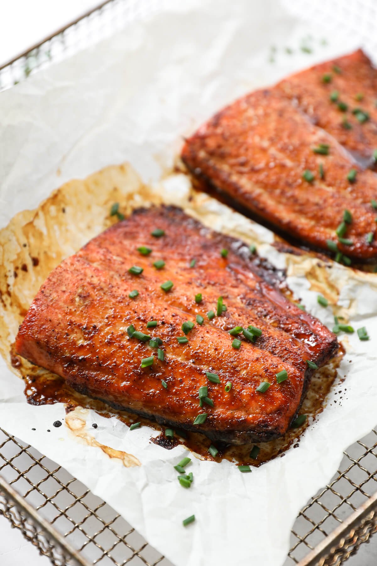 Angled image of air fryer salmon with crispy edges and chopped chives sprinkled on top.