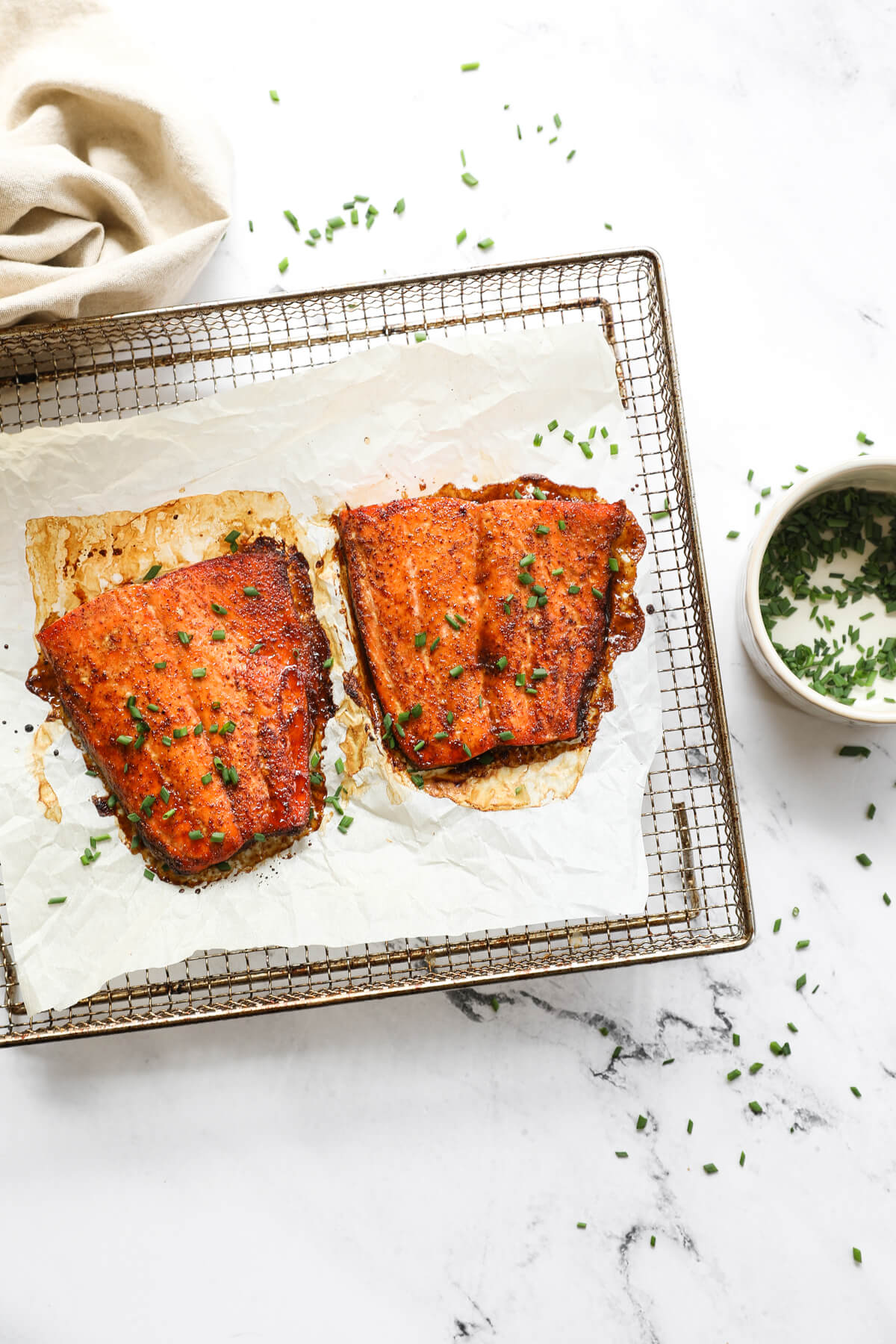 Overhead image of two pieces of salmon cooked in the air fryer with some chopped chives on top and more on the side.