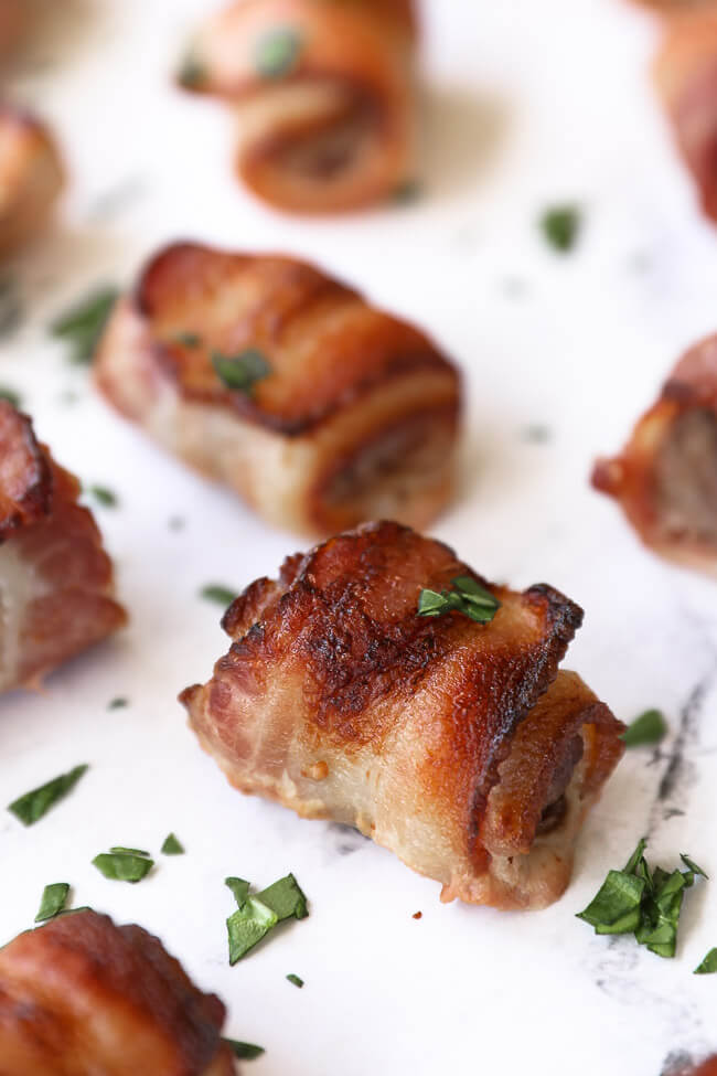 Angled close up image of one piece of steak wrapped in bacon with parsley on top. 