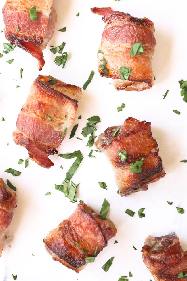 Bacon wrapped steak bites scattered on marble with chopped parsley sprinkled on top. 