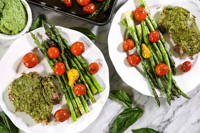 Easy baked pesto chicken on plates with tomatoes and asparagus horizontal image