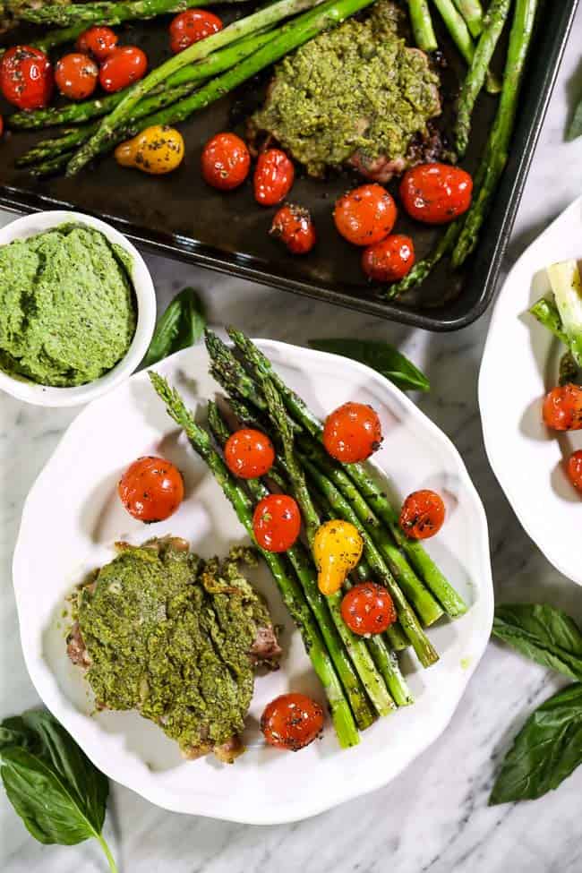 Easy baked pesto chicken on single plate with tomatoes and asparagus sheet pan on top of image