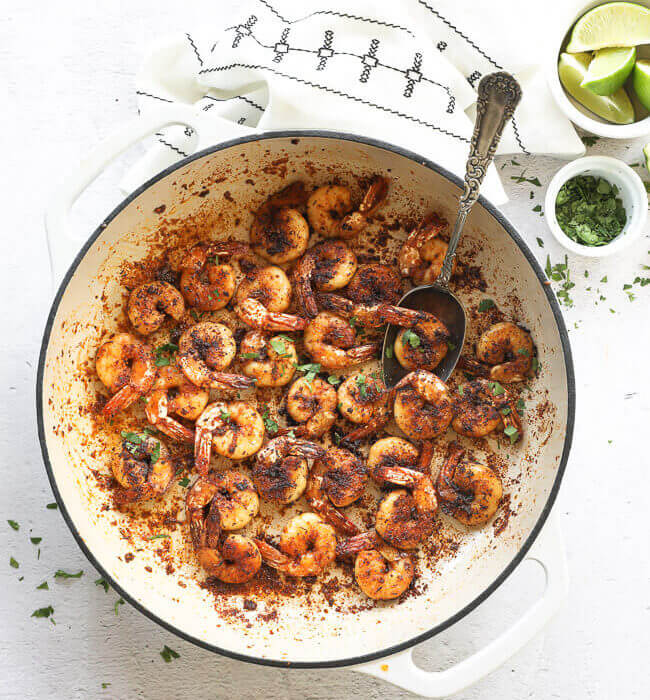 Overhead vertical image of blackened shrimp in a skillet with fresh chopped cilantro sprinkled on top and a spoon like it's scooping shrimp out.