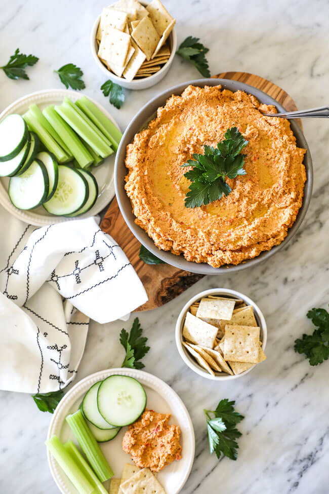 Easy cauliflower hummus in bowl with veggies and crackers spread out on marble vertical pic