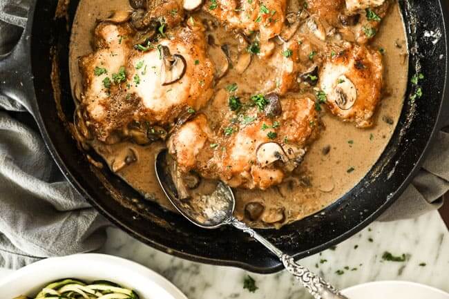 Easy chicken marsala with chicken, mushrooms and a creamy sauce in a cast iron skillet with a serving spoon in the pan. Fresh chopped parsley sprinkled on top. 