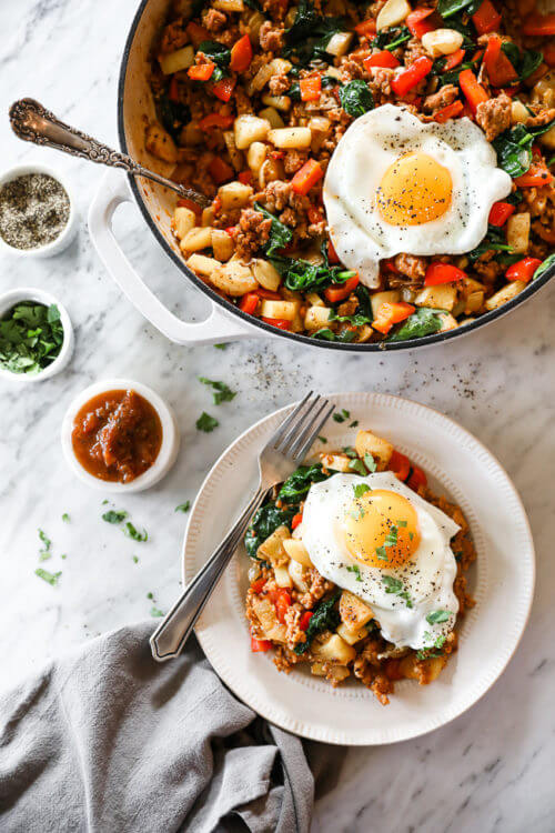 Vertical overhead image of easy chorizo hash in skillet with serving spoon and served up on a plate with a fried egg on top. Salsa, cilantro and pepper on the side.