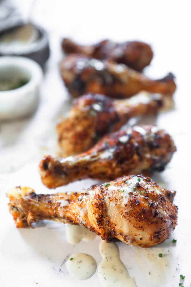 Angled image of chicken drumsticks in a line on marble with ranch drizzled on top. 