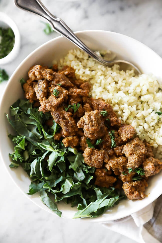 Close up image of easy curry beef in a bowl with greens and cauliflower rice. 