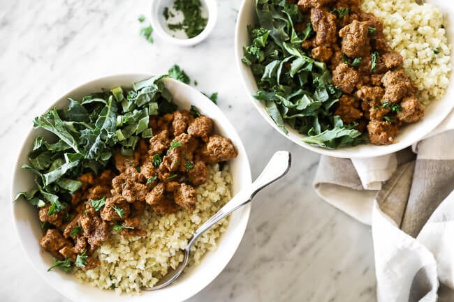 Easy curry beef bowls recipe served up in two bowls with green and cauliflower rice with forks dug into bowls. Chopped parsley on the side. 