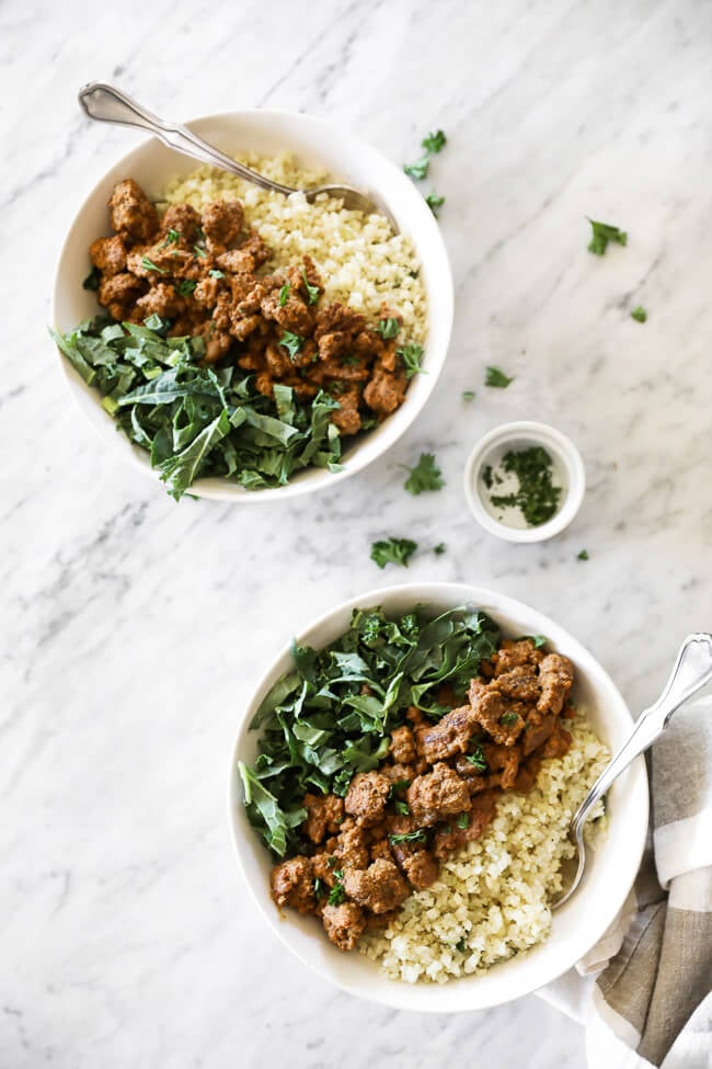Two bowls of easy curry beef with cauliflower rice and greens and chopped parsley on the side. Forks dug into bowls. 