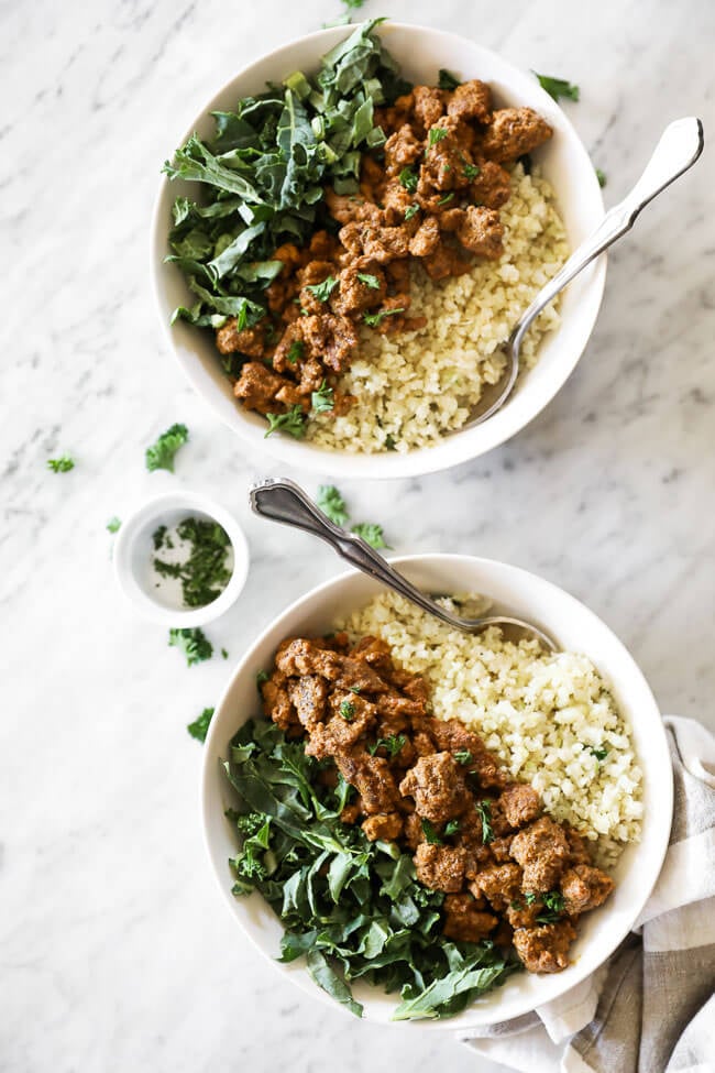 Two bowls of this easy curry beef recipe with greens and cauliflower rice. Topped with chopped parsley and forks dug into bowls. 
