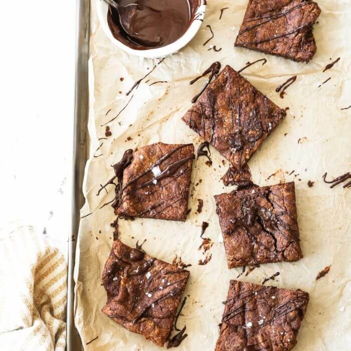 Vertical overhead image of dairy free brownies spread out on a sheet pan with a small bowl of melted chocolate on the side.