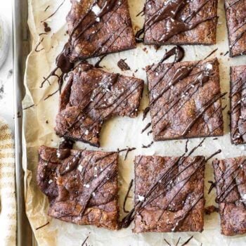 Vertical overhead image of flourless brownies sliced into squares and drizzled with melted chocolate on top. Also sprinkled with flaky sea salt.