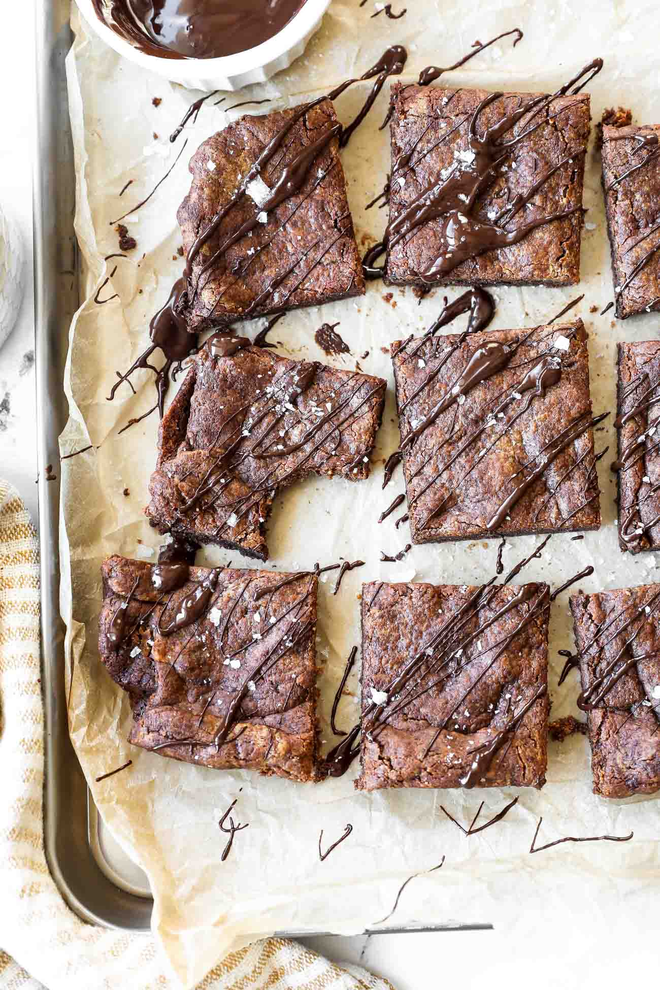 Vertical overhead image of flourless brownies sliced into squares and drizzled with melted chocolate on top. Also sprinkled with flaky sea salt.