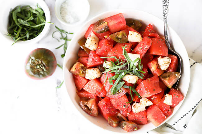 Tomato watermelon salad in a bowl with a serving spoon. Topped with fresh chopped basil. 