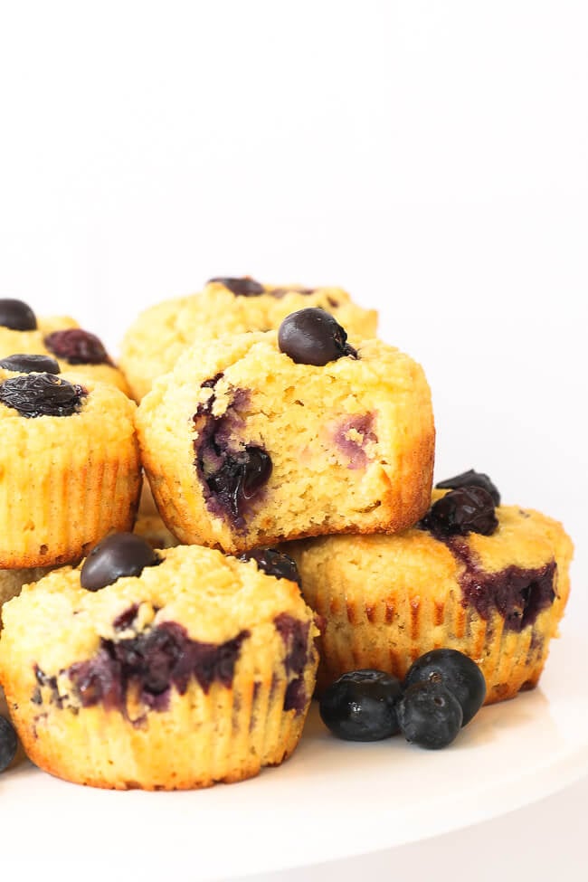 Gluten free lemon blueberry muffins on a cake stand with one muffin having a bite taken out of it. 