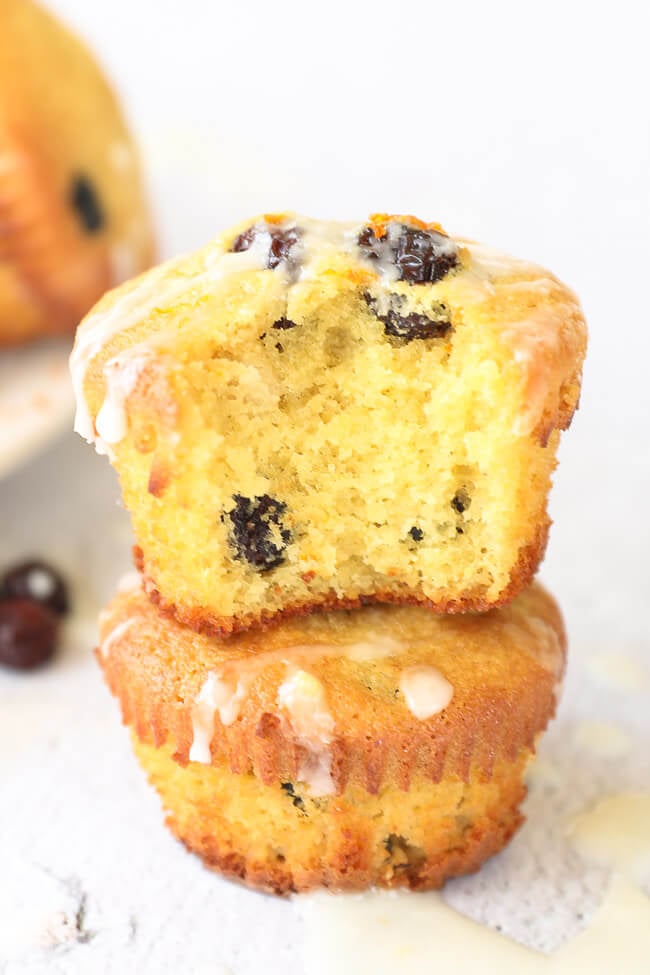 Close up of two orange cranberry muffins stacked. Top muffin has a  bite taken out of it. 