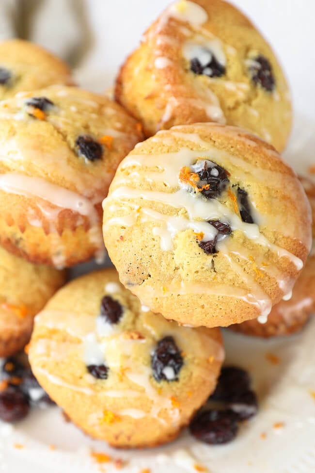 Close up angled shot of stacked orange cranberry muffins on plate. Orange icing drizzled on top. 