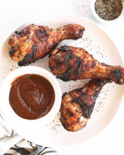 Grilled chicken drumsticks on a plate with BBQ sauce and pepper