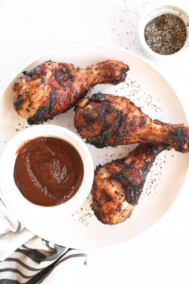 Grilled chicken drumsticks on a plate with BBQ sauce and pepper