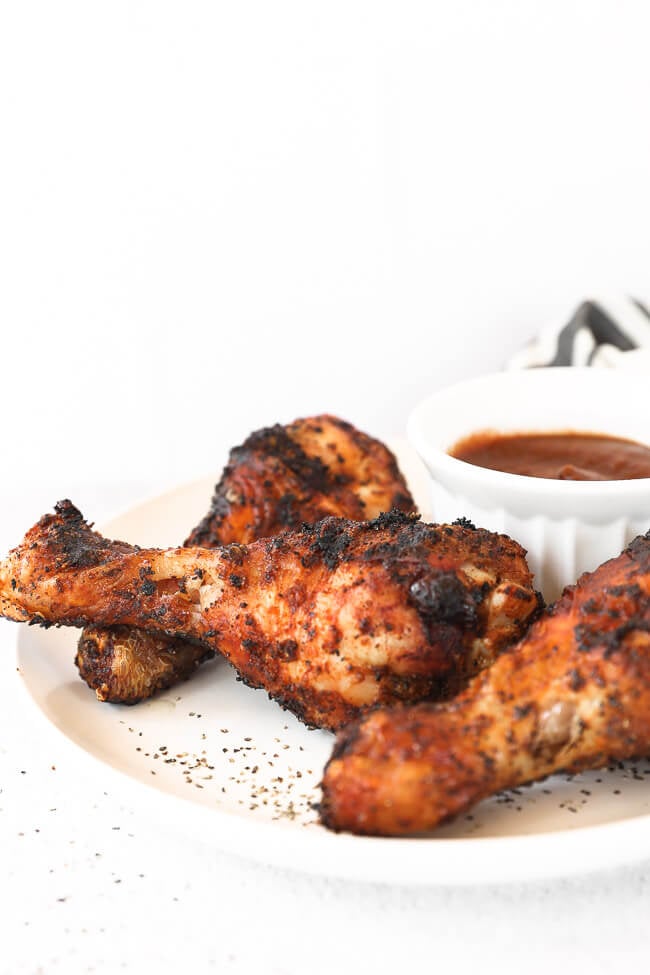 Grilled chicken drumsticks on a plate with BBQ sauce in background close up angle image