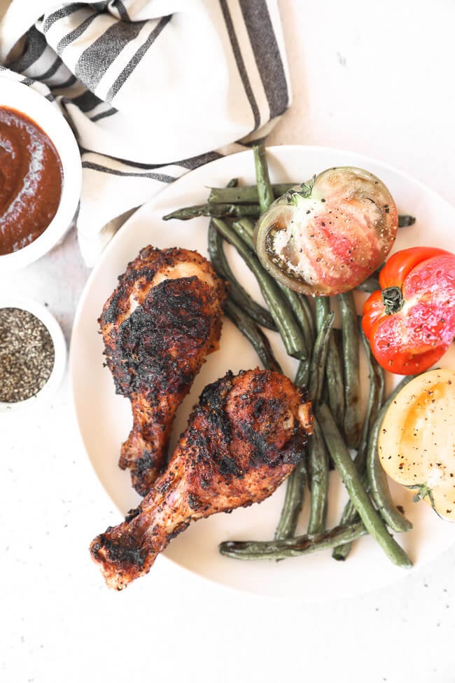 Des pilons de poulet grillés sur une assiette avec des haricots verts et des tomates