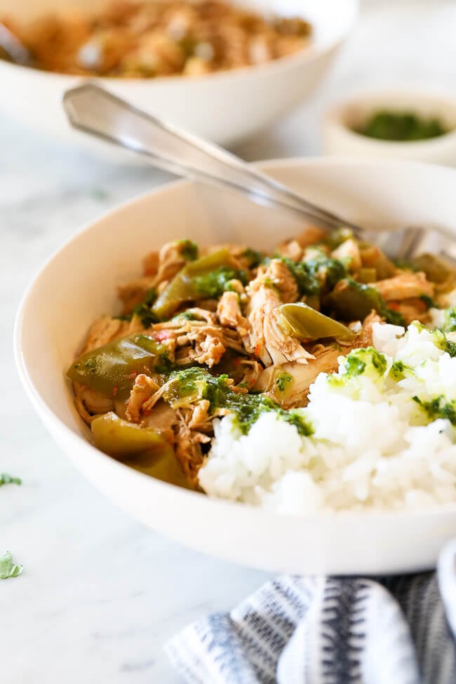 Angled image of easy harissa chicken in a bowl with rice and fork dug in. Green sauce drizzled on top. 