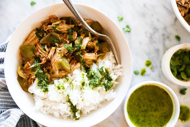 Easy harissa chicken recipe served in a bowl with white rice and a creamy herb sauce drizzled on top. Extra sauce and cilantro on the side. 