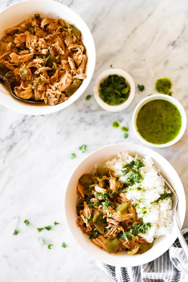 Easy harissa chicken recipe served in a bowl with white rice and a creamy herb sauce drizzled on top. Extra sauce, cilantro and chicken all on the side. 